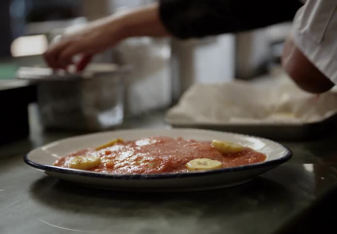 Woman working in a commercial kitchen garnishes a steaming meal
