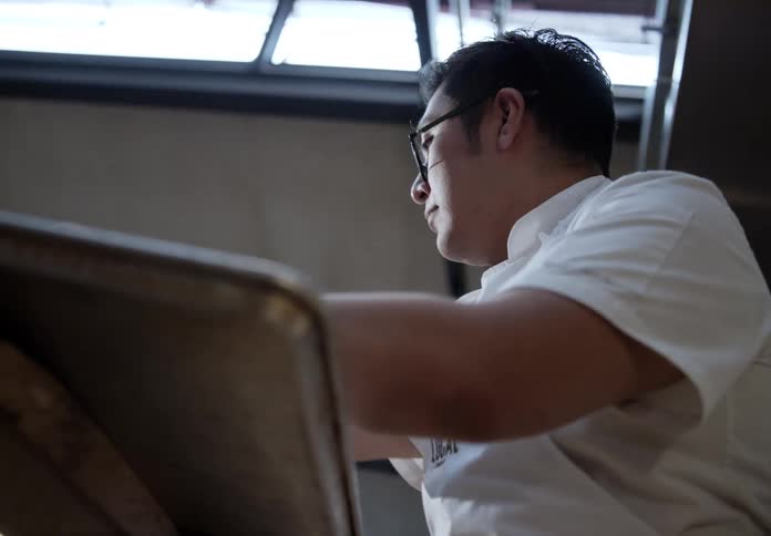 The face of a man with glasses picking something up and letting go of a table in front of him