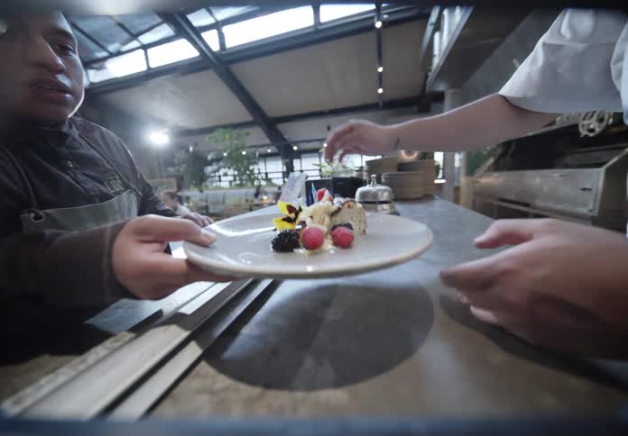 Chef adding final touch to dessert with fruits and edible flowers