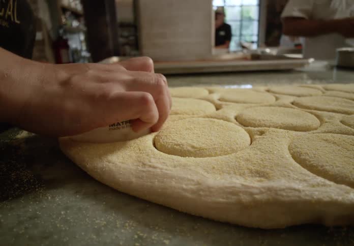 Hand cutting dough circles with a mold on a floured surface