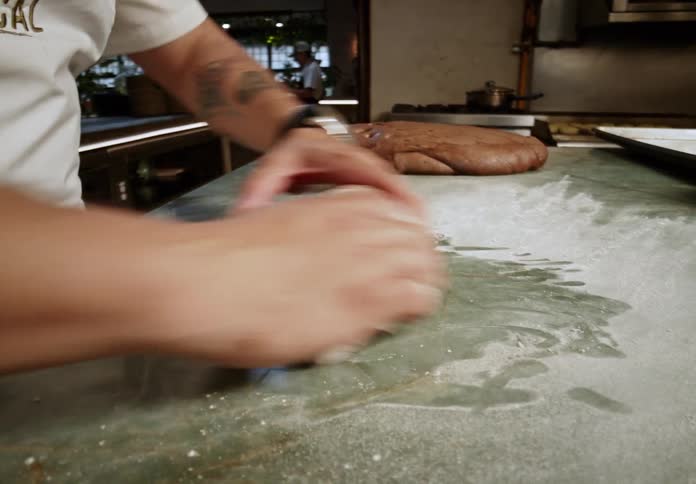 A man rolls bread dough into a loaf while working in a bakery