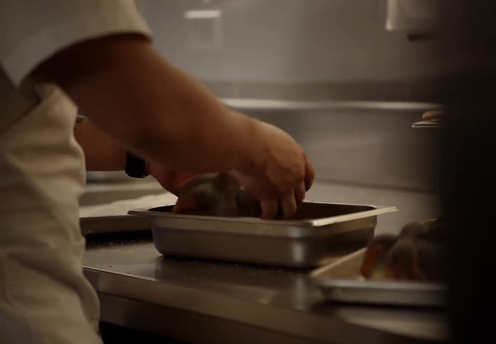 Cook sprinkling sugar over pastries on a metal tray