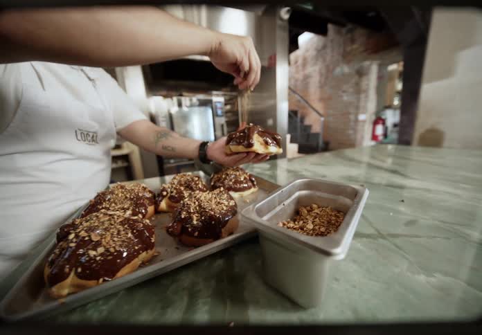 Baker adding chopped nuts over chocolatecovered pastries