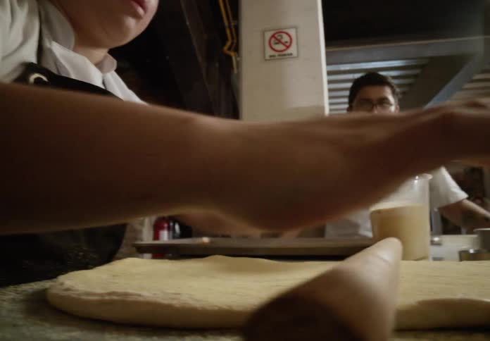 Baker sprinkling flour over dough while a coworker watches