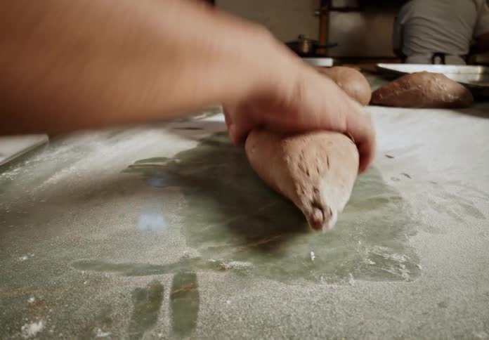A man rolls bread dough into a loaf while working in a bakery