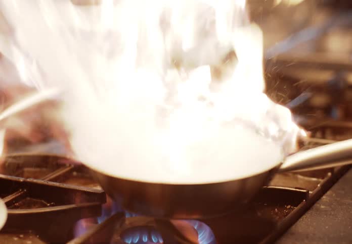 Intense flame surrounding a frying pan on a lit stove