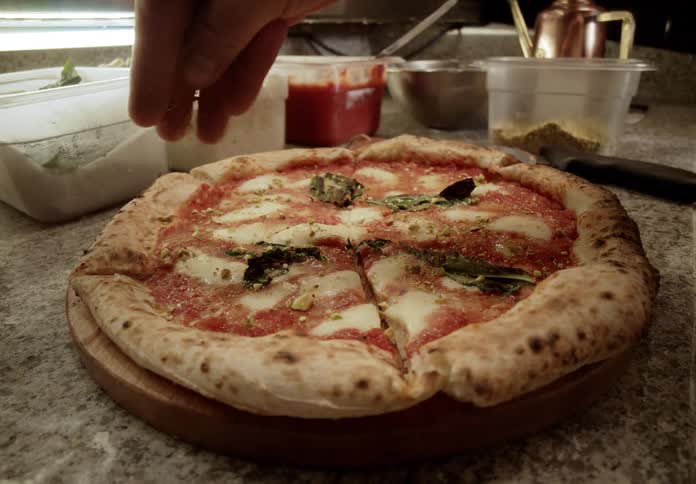 Man slices a pizza then spreads a topping on to it