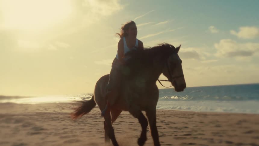 A woman riding a horse beside a beach on a clear morning