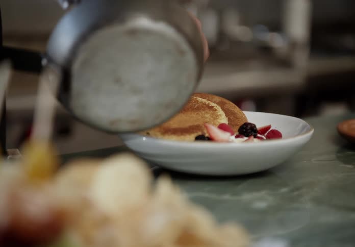 Hand finishing pancakes with fresh fruits on a white plate