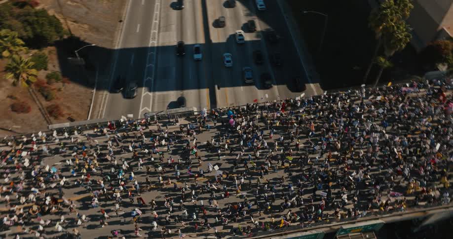 A massive crowd of people marches across a bridge over a busy freeway