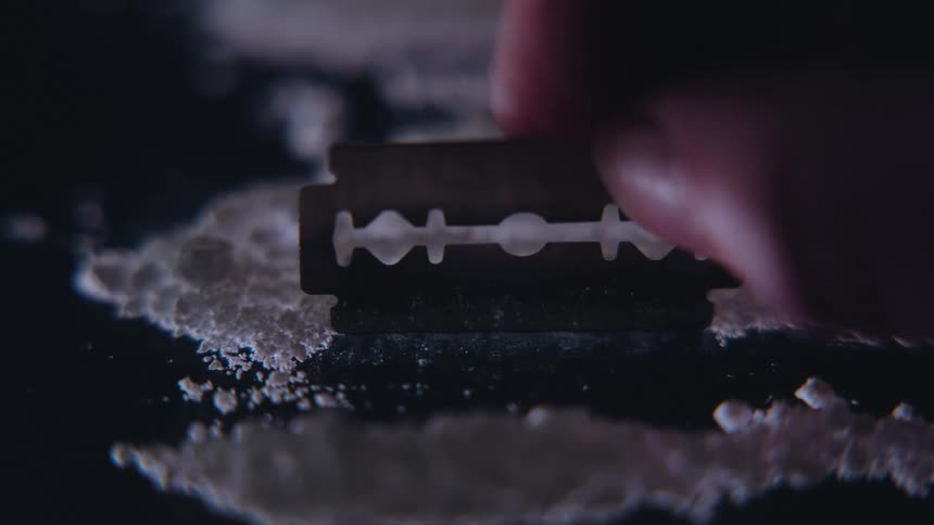 Hand with a razor blade dividing white powder