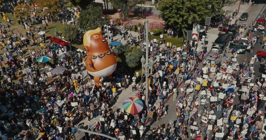 Protesters with a large anti trump balloon fill an urban intersection on a fall day