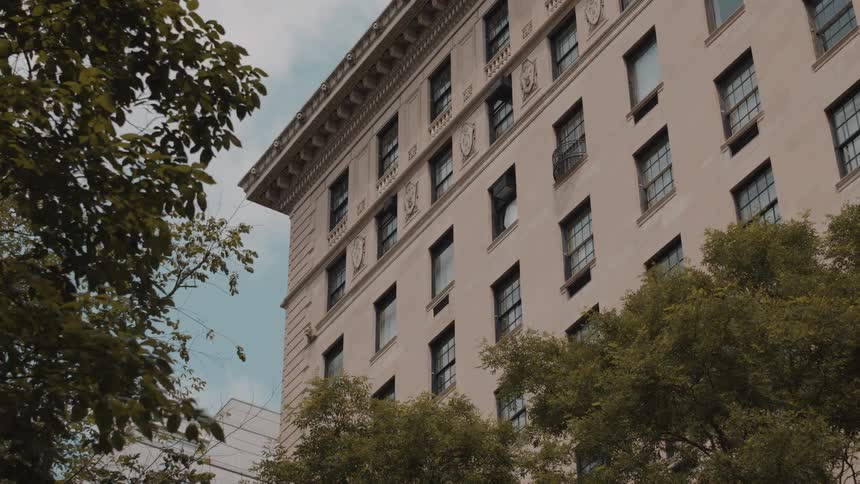 A stately apartment building is partially obscured by leafy trees under a slightly cloudy sky