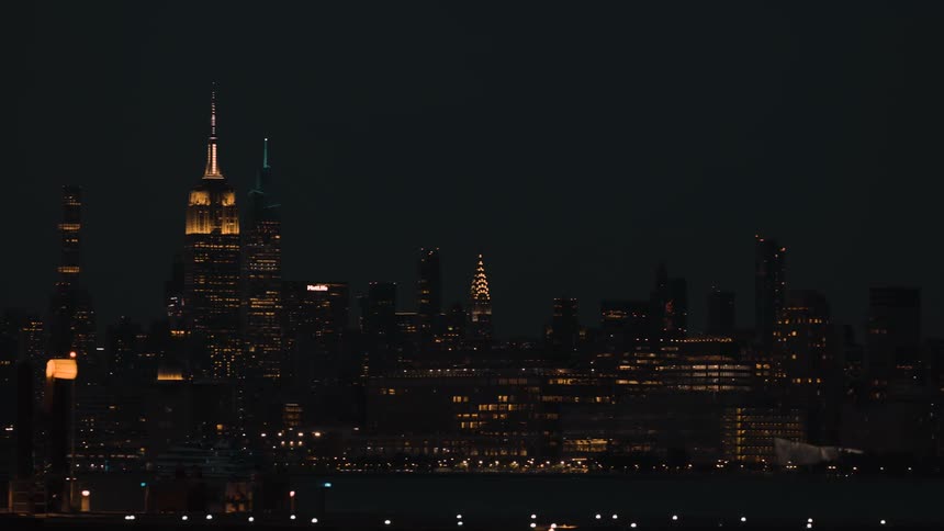 Lights glow on metropolitan towers and skyscrapers as people walk along the coast