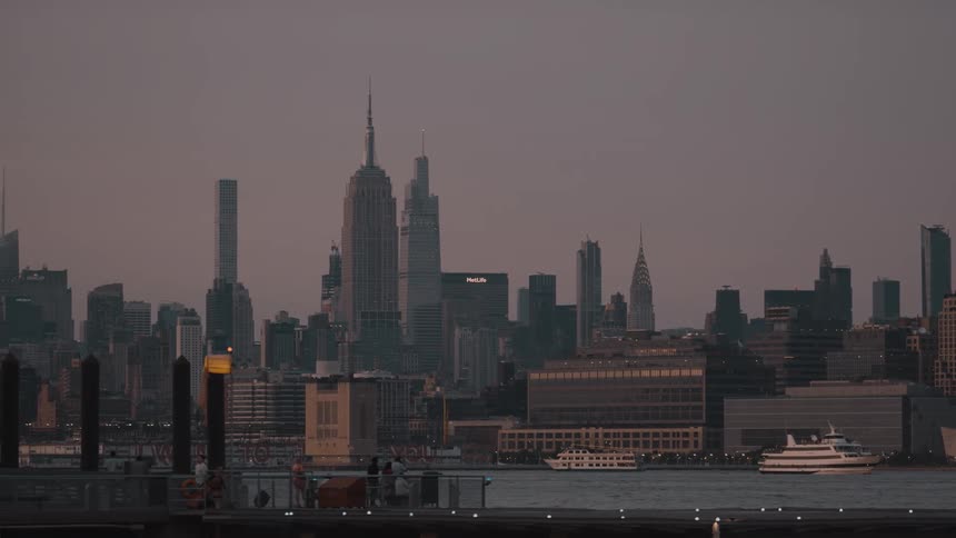Boats sail in front of the city skyline under the soft evening light