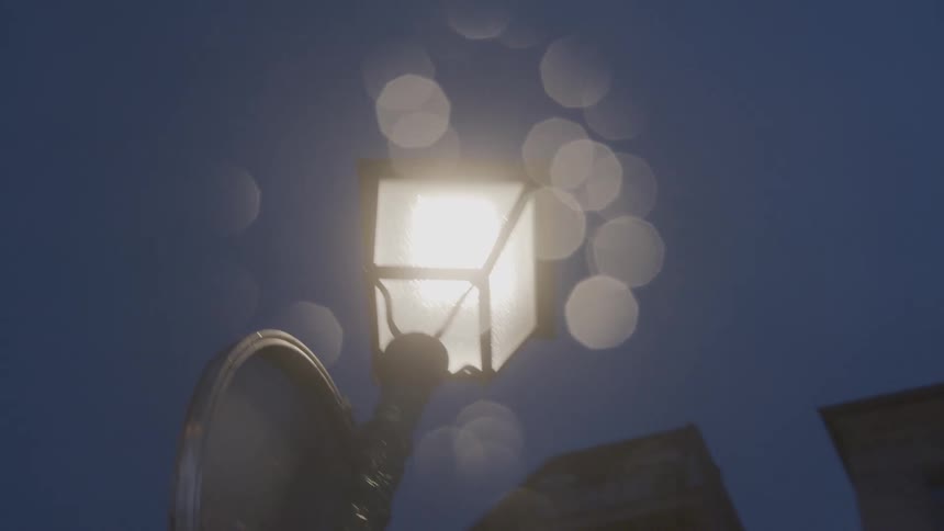 A glowing street lamp shines against the deep blue twilight sky as shimmering outoffocus rain droplets drift past the light