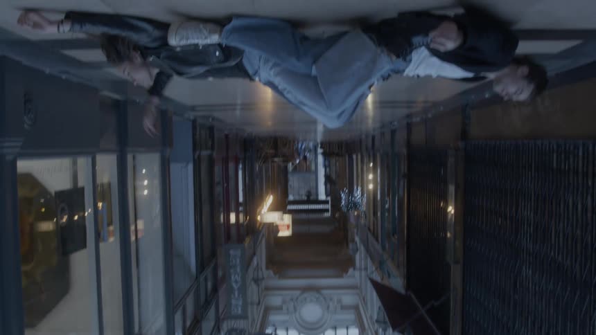 The glass ceiling of an elegant arcade gives way to a surreal upside down scene of a couple lying on the floor moving into a romantic sitting position