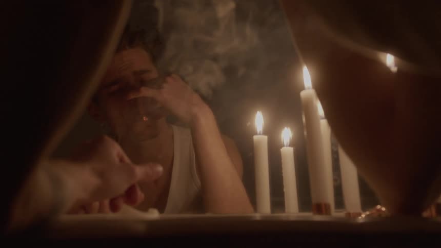 The man is smoking in front of a mirror