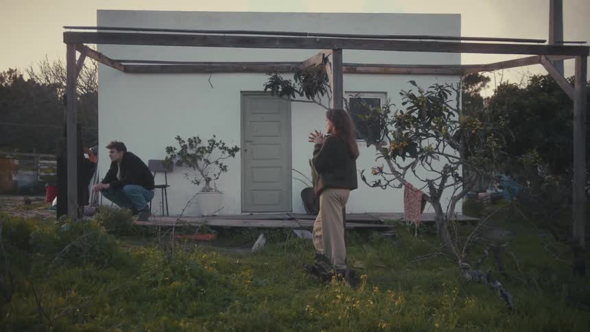 The man is crouching by the small home