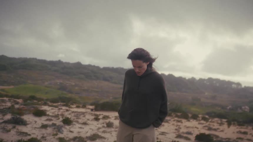 The woman is pacing in the sand on a windy day