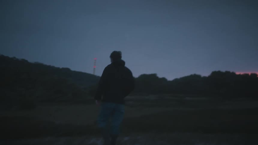 Man walks alone at dusk toward distant lights