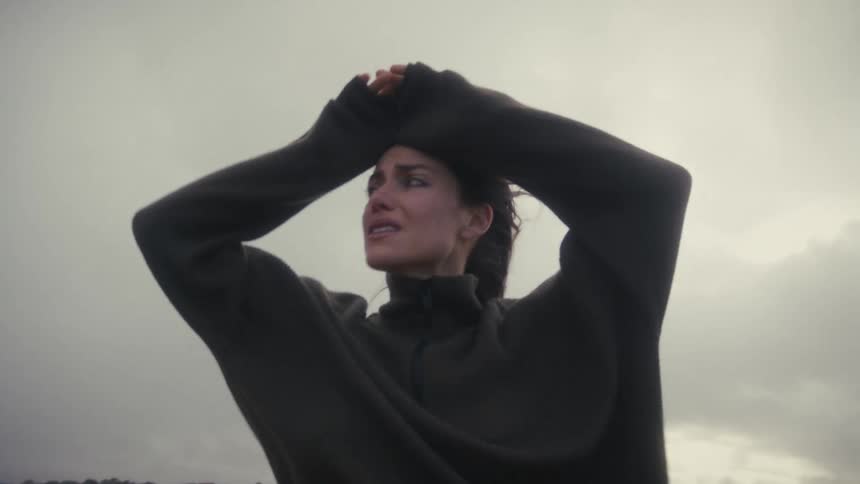 Woman cries with hands on her head under a gray sky