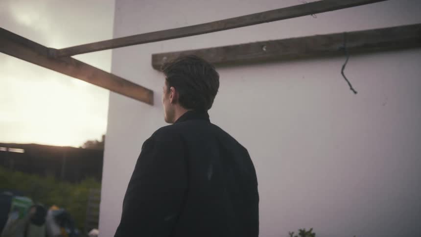 Young man stands outside next to a building moving his arms and walking as he talks