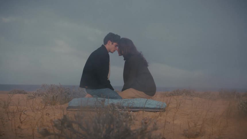 Couple sitting face to face amid an arid landscape under a cloudy sky