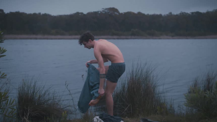 Man taking off his pants by the edge of a lake