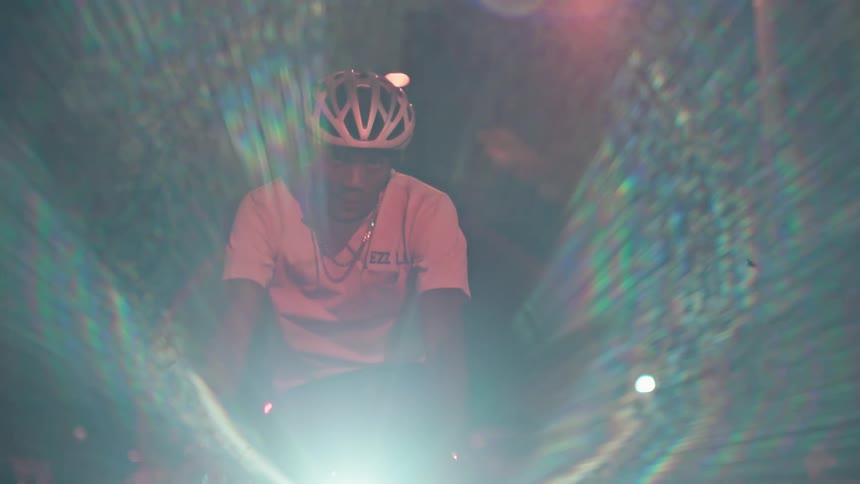 A cyclist wearing a helmet and a lightcolored shirt riding towards the camera in darkness with the scene dominated and obscured by a powerful brilliant white light source at the bikes front