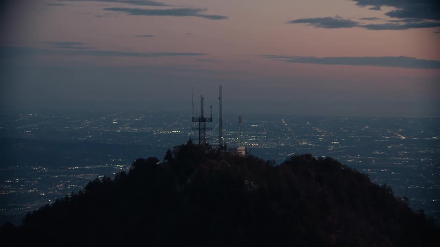 Communication towers on a hilltop overlooking the city at dusk
