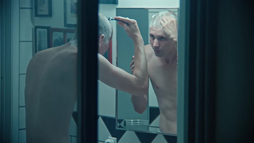The man is shaving his head in the bathroom