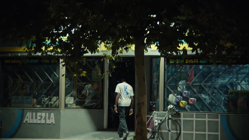 Young man walks his bicycle out of a downtown store as traffic passes on the street