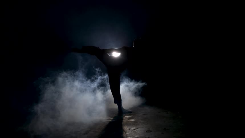 A man is doing a martial arts kick in the dark