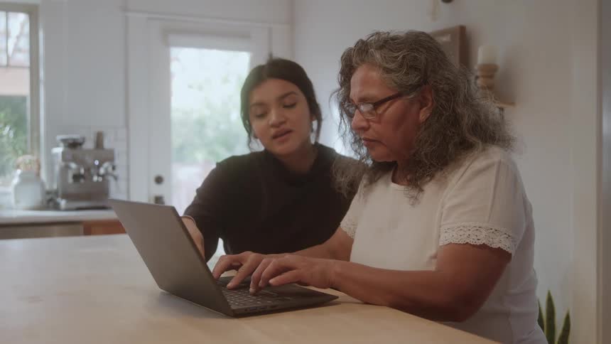 The teenager talks with her mother as she types on a laptop