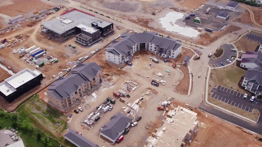 Aerial view of cars and trucks parked at a neighborhood construction site with workers on the roof of a building
