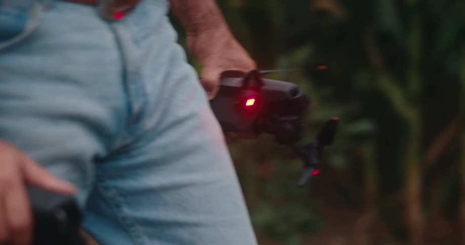 A man is walking next to a cornfield holding a drone in one hand and the controller in his other hand