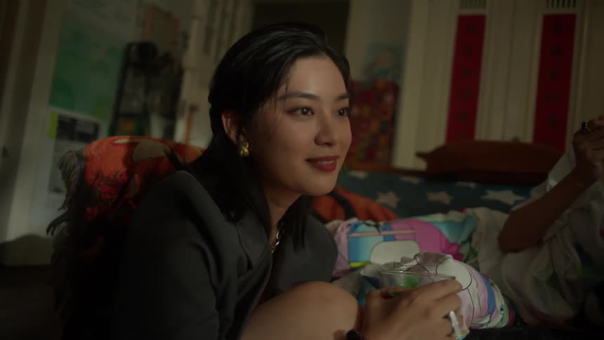A young woman smiles and chats with her friend as they relax and eat snacks together in a cozy room