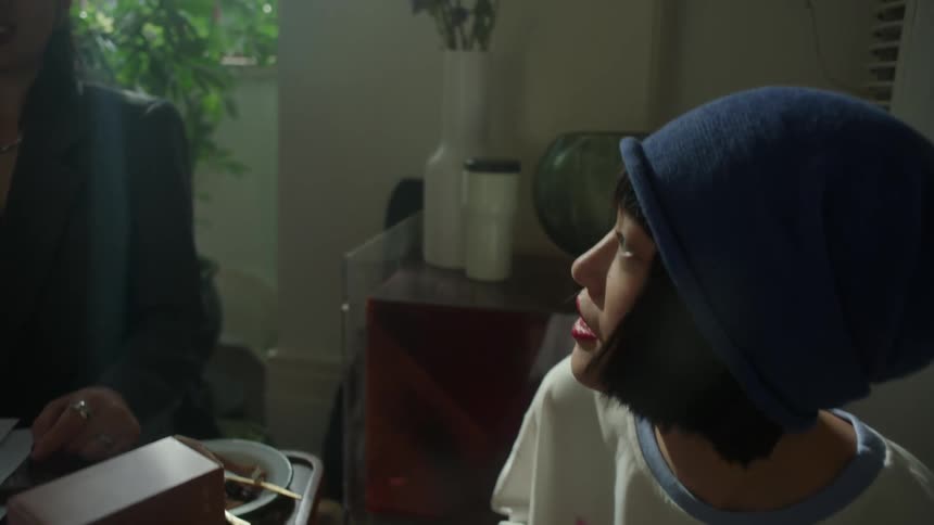 A man feeds a bite of his food to a woman sitting in a room with a lot of plants