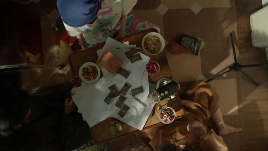 A diverse group of young adults women reclining casually on the floor and cushions around a small low table covered with papers snacks and a professionalgrade microphone with the womans laughing