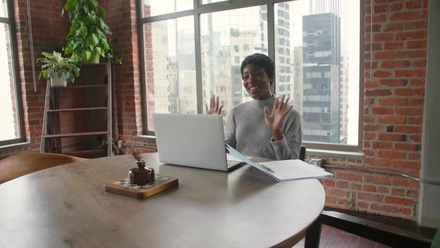 Woman sitting at a table near a window having a conversation on a laptop computer