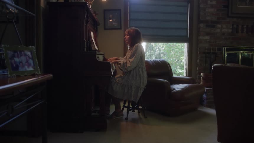 Woman sits in her living room during the day and plays the piano