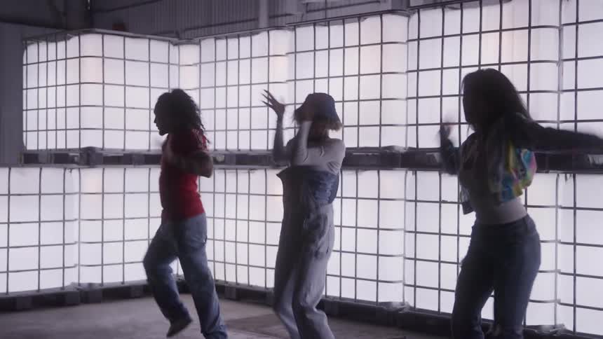 Group dances in front of illuminated panels inside a warehouse