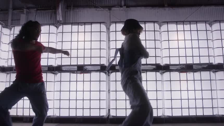 Three women are dancing indoors with several bright blocks of light behind them and they are partially dark