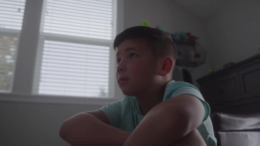 Boy sits hugging his legs while looking at something ahead