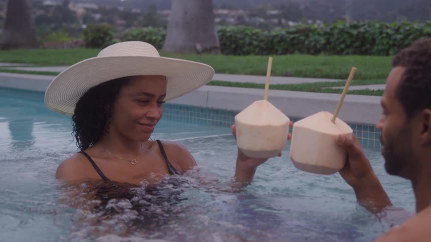 Couple toasts with coconuts while standing in a pool