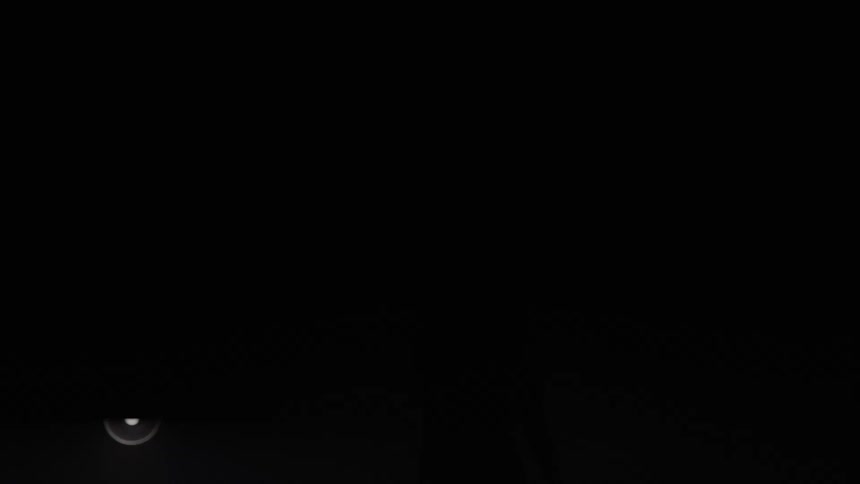 The dark silhouette of a woman with long hair moving energetically on a stage framed against a blindingly bright foggy background punctuated by a symmetrical array of glowing circular white lights