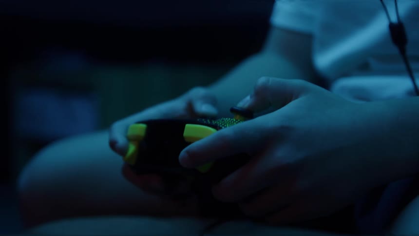 Hands hold a video game controller lit by blue light