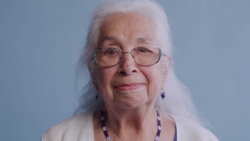 Elderly woman with white hair smiles gently against a blue background