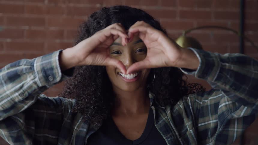 Woman smiles and makes the shape of a heart with her hands